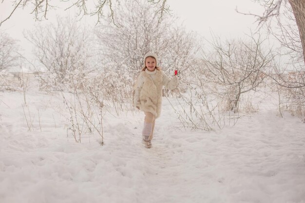una chica con un sombrero de punto blanco y un suéter con un caramelo en las manos en un parque nevado