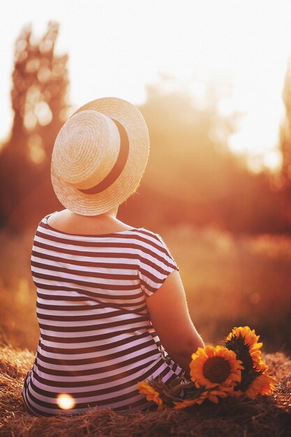 La chica con un sombrero con un ramo de girasoles posa.