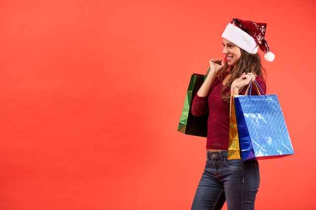 Foto chica con sombrero de santa claus sonriendo con bolsas de compras de navidad sobre fondo naranja