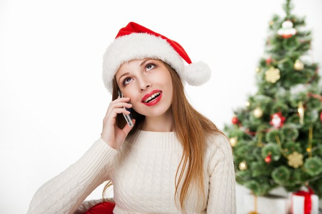 Chica con sombrero de santa llamada teléfono por árbol de Navidad