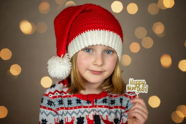 Una chica con un sombrero de santa tiene un cartel de feliz año nuevo en un fondo bokeh de año nuevo