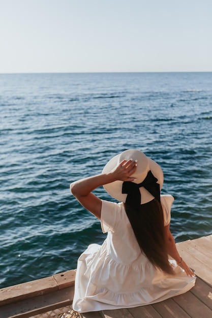 chica con sombrero sentada cerca del mar