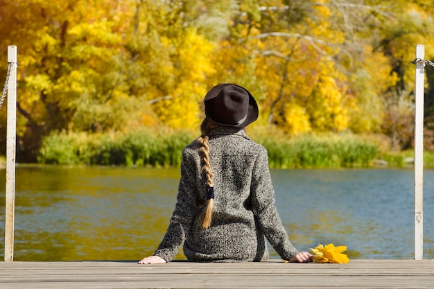 Chica en el sombrero sentado en el muelle Día de otoño Vista posterior