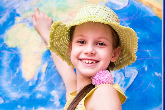 La chica del sombrero sonríe y muestra el mapa mundial.