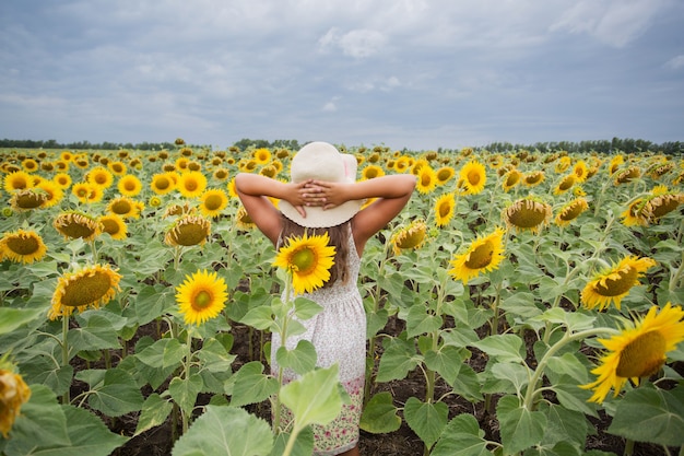 Chica con sombrero de verano de pie en el campo de girasoles