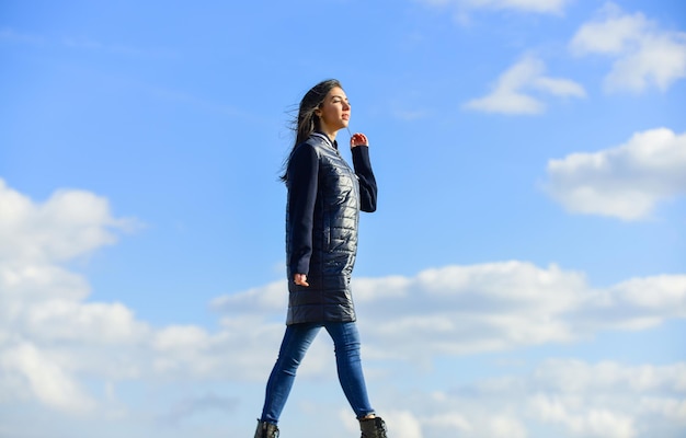 Chica soñadora Concepto joven y libre Espera más de tu ropa Mujer disfruta del clima al aire libre Belleza y moda Caminar sola Mujer sobre fondo de cielo azul Vacaciones de invierno Chaqueta larga abrigo