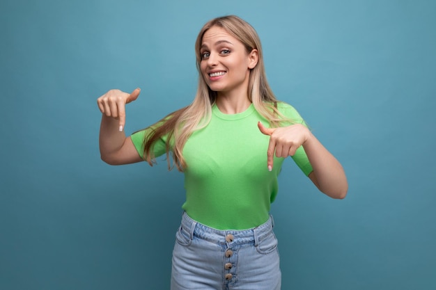 Chica sonriente alegre con ropa informal apuntando hacia abajo a la pancarta en un fondo azul