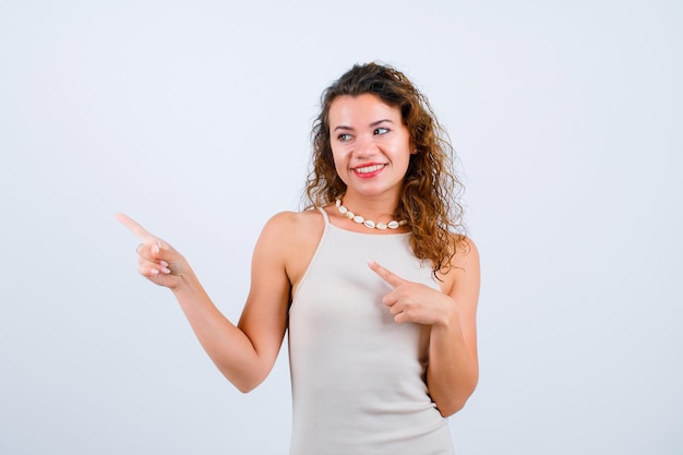 Chica sonriente está mirando y apuntando a la izquierda con los dedos índices sobre fondo blanco.