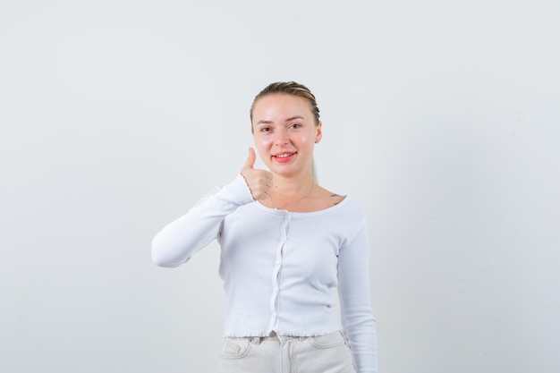 Chica sonriente está mostrando su pulgar sobre fondo blanco.