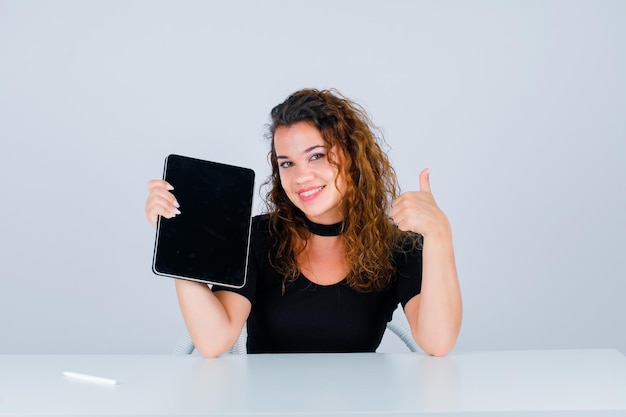 Chica sonriente está sosteniendo la tableta y mostrando un getsure perfecto sobre fondo blanco.