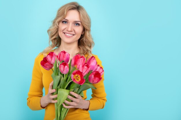 Chica sonriente con flores de tulipán de primavera sobre fondo azul.