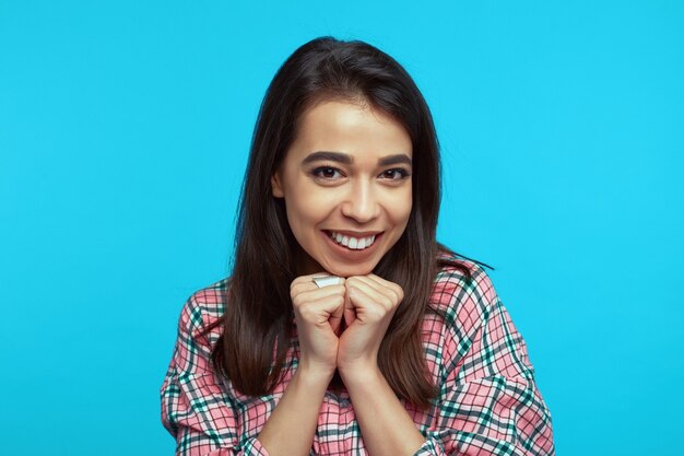 Chica sonriente optimista junta las manos cerca de la cara sonríe ampliamente vestida con