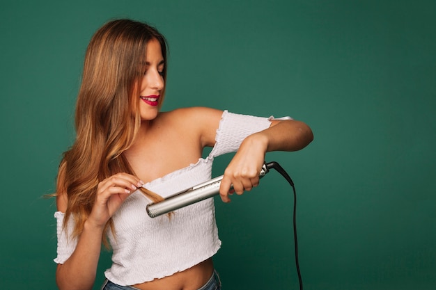 Foto chica sonriente con plancha para el pelo