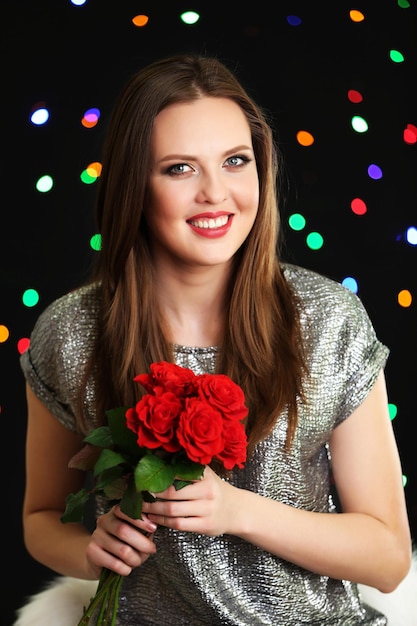 Chica sonriente con ramo de rosas rojas sobre fondo de luces