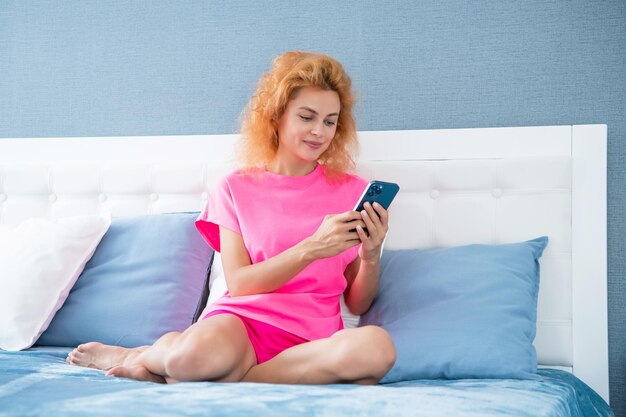 chica sonriente relajarse en casa y los mensajes de texto en el teléfono chica mensajes de mensaje en el teléfono en la cama teléfono mensajes de texto de la chica