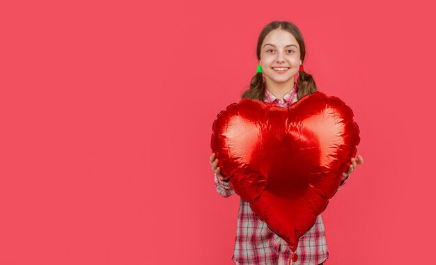 Una chica sonriente sostiene un globo de corazón de amor sobre un fondo rojo