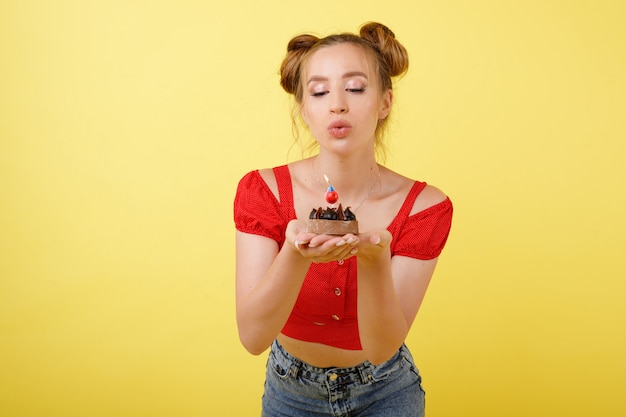 Chica sopla una vela en el pastel en un espacio amarillo. Fiesta. Feliz cumpleaños a ti