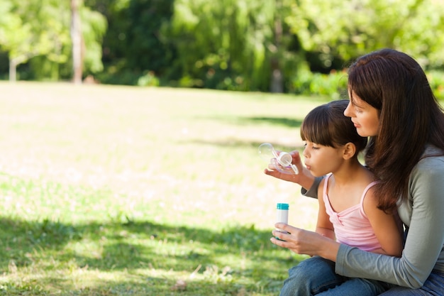 Chica soplando burbujas con su madre en el parque