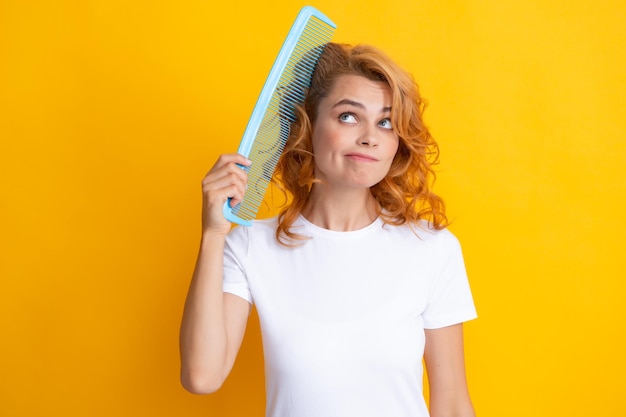 Chica sorprendida asombrada peinando el cabello Mujer pelirroja con un peine aislado sobre fondo amarillo Chica