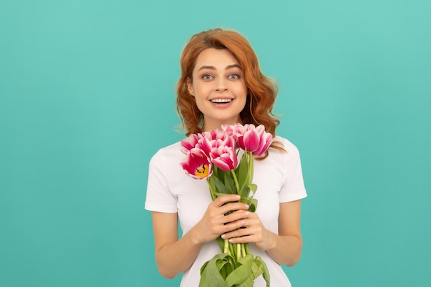 Chica sorprendida con ramo de flores de tulipán sobre fondo azul.