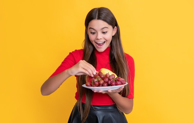 Una chica sorprendida sostiene un plato de fruta fresca con fondo amarillo