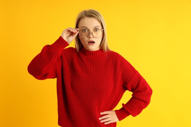 Chica sorprendida en suéter y gafas sobre fondo amarillo.