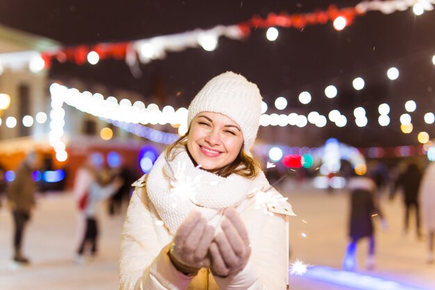 Chica sosteniendo una bengala en la mano. Fondo de ciudad de invierno al aire libre, nieve, copos de nieve.