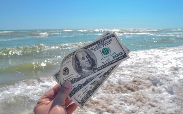 Chica sosteniendo un billete de 300 dólares en el fondo de las olas del mar