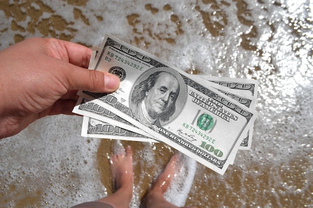 Chica sosteniendo un billete de 300 dólares en el fondo de las olas del mar