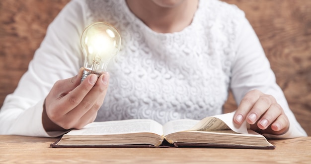 Chica sosteniendo bombilla y libro de lectura. Conocimiento, Creatividad, Sabiduría