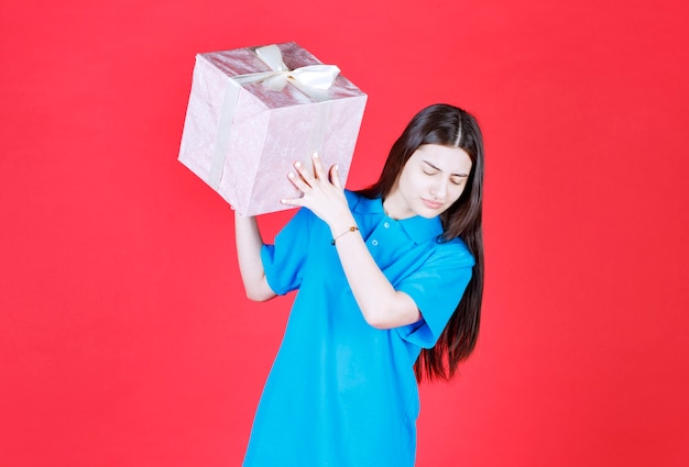 Chica sosteniendo una caja de regalo violeta envuelta con cinta blanca.