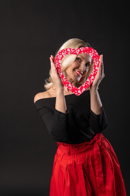 Chica sosteniendo un corazón a la altura de los ojos rojo coqueteando en el suelo corazones boda inspiración banner amor