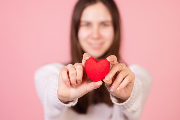 Chica sosteniendo un corazón en sus manos primer plano sobre un fondo rosa el concepto del día de san valentín