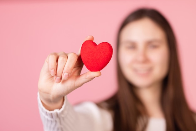 Chica sosteniendo un corazón en sus manos primer plano sobre un fondo rosa el concepto del día de san valentín