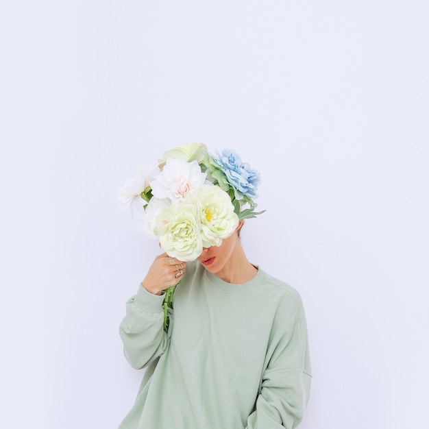 Chica sosteniendo flores delante de su cara con un estilo ecológico informal y elegante