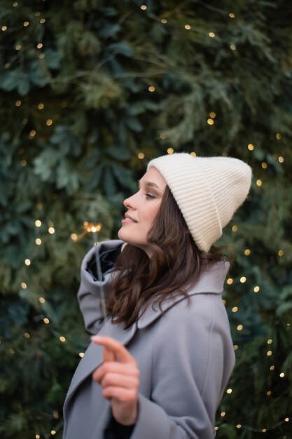 Foto chica sosteniendo fuego de bengala cerca del árbol de navidad concepto de vacaciones estado de ánimo de invierno