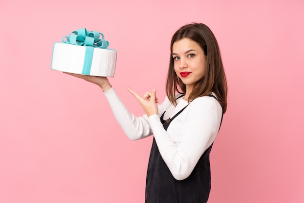 Chica sosteniendo un gran pastel en rosa y señalando