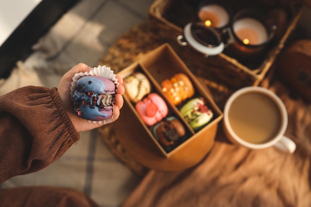 Chica sosteniendo un macaron en la mano con una caja de macarons variados en el fondo en un ambiente hogareño acogedor