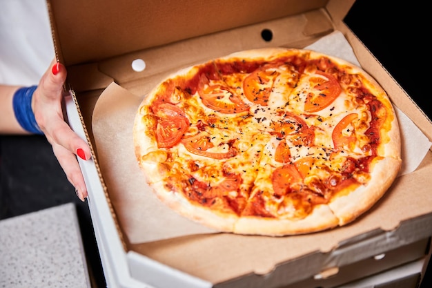 Chica sosteniendo una pizza en una caja abierta preparándola para la entrega