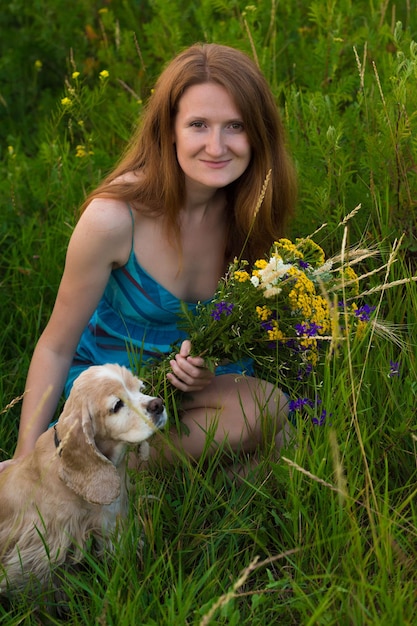 Chica sosteniendo un ramo de flores silvestres sentado en el campo con su perro