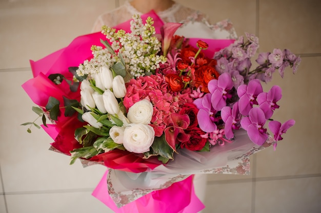 Chica sosteniendo un ramo de tulipanes blancos y lilas, orquídeas rosadas y hortensias y rosas rojas