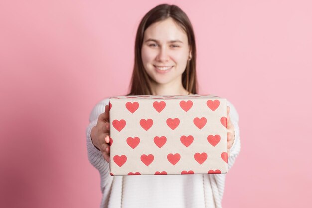 Chica sosteniendo regalo con corazones sobre fondo rosa concepto de día de san valentín