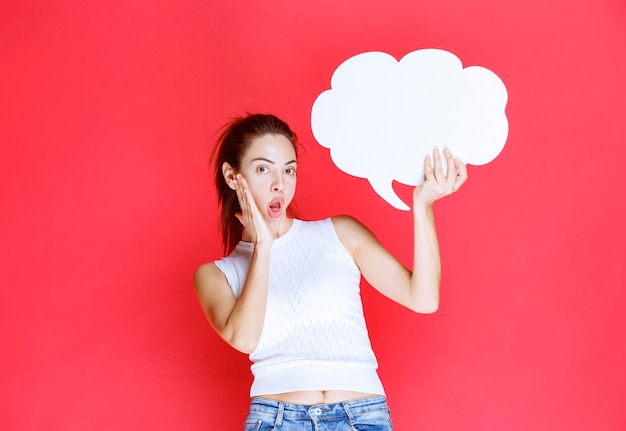 Chica sosteniendo un tablero de ideas en forma de nube en blanco y parece sorprendida.