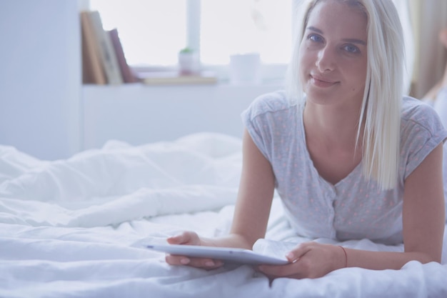 Chica sosteniendo tableta digital con pantalla en blanco y sonriendo a la cámara en el dormitorio