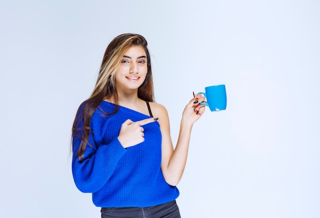 Chica sosteniendo una taza de café azul y mostrando a alguien.