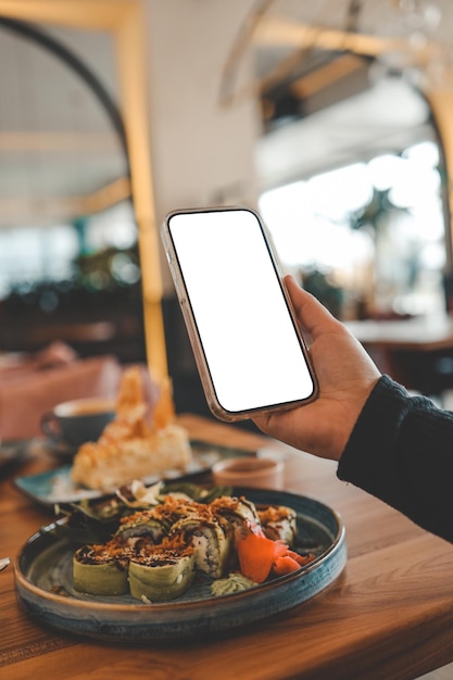 Foto chica sosteniendo un teléfono con una pantalla en blanco en un café con comida de fondo