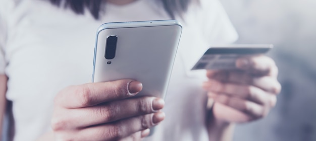 Chica sosteniendo un teléfono y una tarjeta bancaria en sus manos