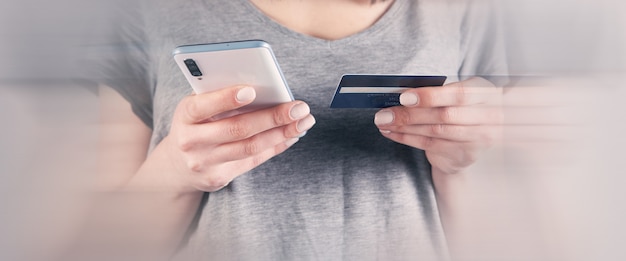 Chica sosteniendo un teléfono y una tarjeta bancaria en sus manos