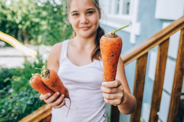 Chica sosteniendo una zanahoria en sus manos. Cosecha, alimentación saludable.