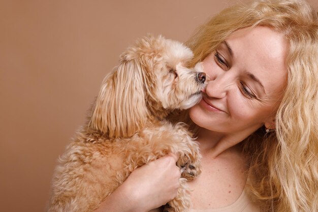 Foto una chica sostiene un lindo perro maltipoo en sus brazos primer plano en un fondo beige plano el concepto de amor por un perro